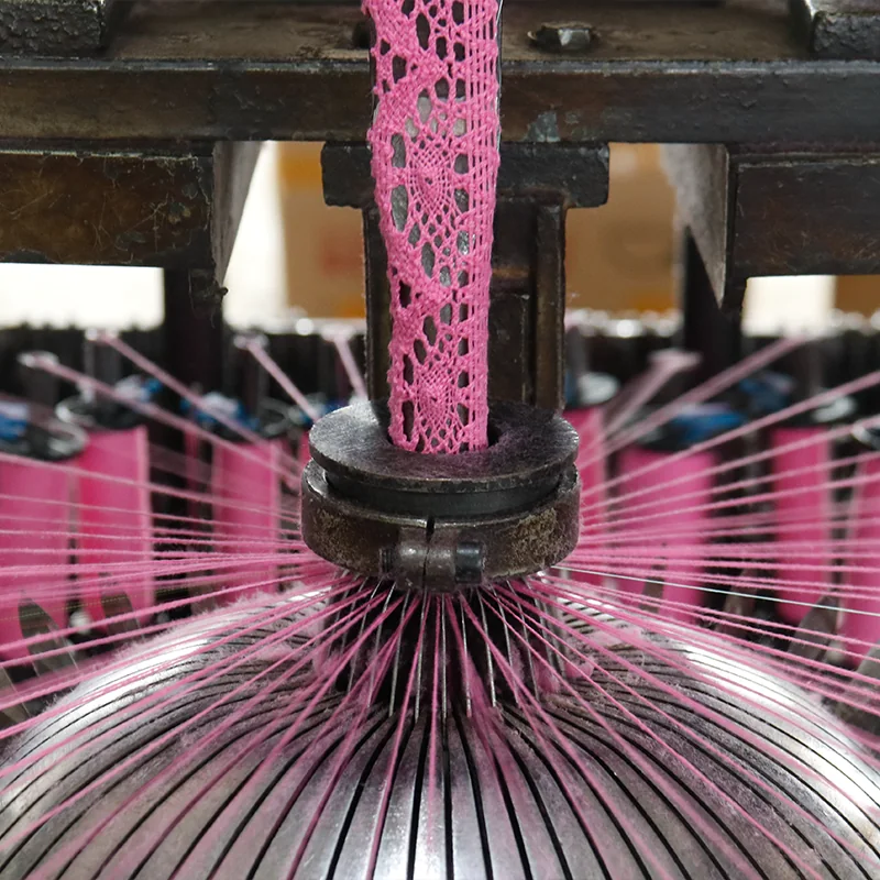 Start production Bright pink threads feeding a machine as a strip of pink lace takes shape.