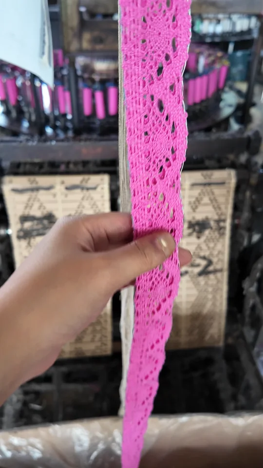 Check your sample A hand holding bright pink lace to show its floral pattern, openwork and edge.